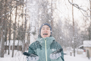 Teenager girl throwing snow in the air and having fun during winter holidays in a snowy forest