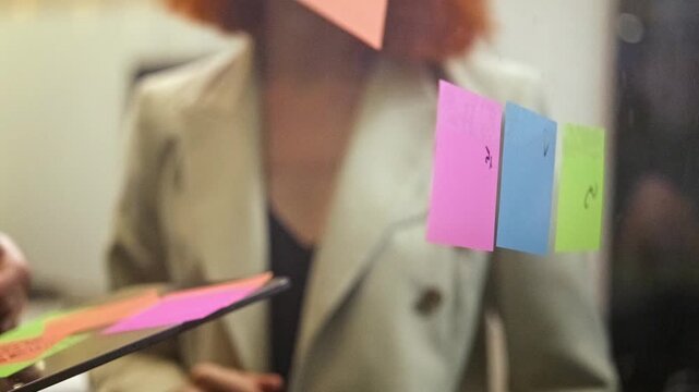Close-up of team brainstorming with sticky notes on glass during planning meeting. Modern office workshop shows collaboration, strategy, methodology, startup energy, and corporate teamwork. 4k video