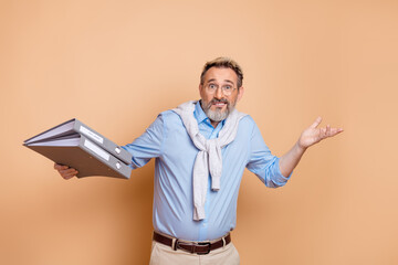 Mature businessman with a thoughtful expression holding binders and gesturing on a beige background for advertising uses