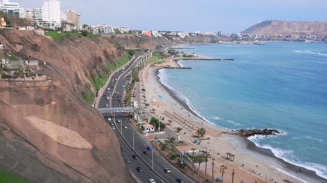 Vehicles driving along the costa verde highway beside miraflores beach with paragliding in the distance