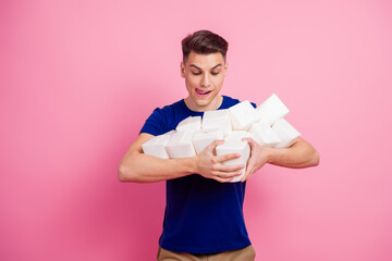 Young man in blue shirt holding many takeout boxes against pink background representing fun and casual lifestyle