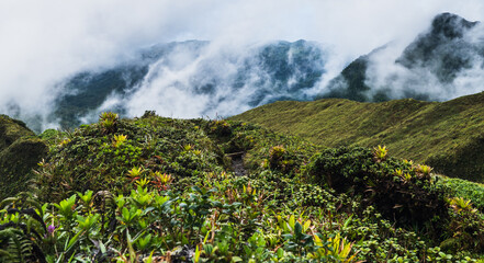 Vibrant Green Mountain Overlooking Mist Wreathed Hills in Daylight Clarity.