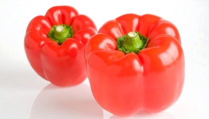 Two vibrant red bell peppers, glossy and plump, sit on a reflective white surface