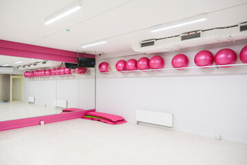 Empty pink gym room interior with fitness exercise balls and mirrors. Workout studio with training equipment for sport and yoga class.