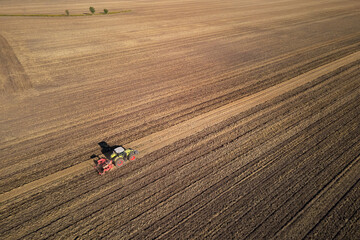 Green tractor with machinery working on agricultural field, plowing farmland under clear sky, aerial view. Small farming concept