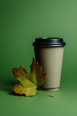 An eco-friendly coffee cup paired with an autumn leaf set against a teal background.