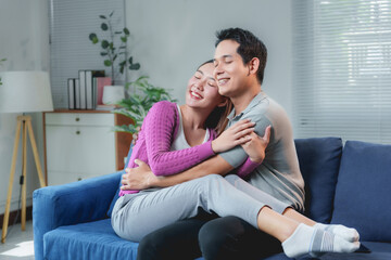 Obraz premium Young asian couple hugging and smiling, enjoying their time together on a comfortable blue sofa in a cozy living room