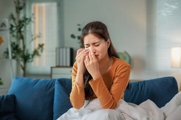 Sad woman sitting on sofa covered with blanket is wiping tears with tissue paper, suffering from depression, grief, stress, pain, having problems, bad relationships or illness