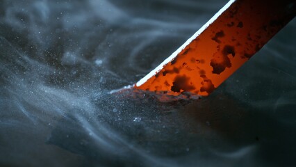 Blacksmith puts the red-hot forged metal part into cold water , close-up
