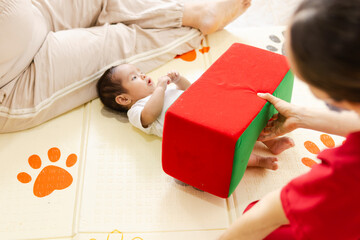 Baby in early stimulation therapy with physiotherapist guiding exercises with foam block, concept of child development and care