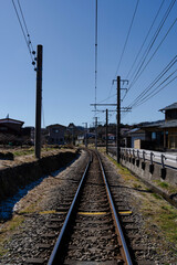 Train tracks disappear into the distance, curving through a rural landscape under a clear blue sky.