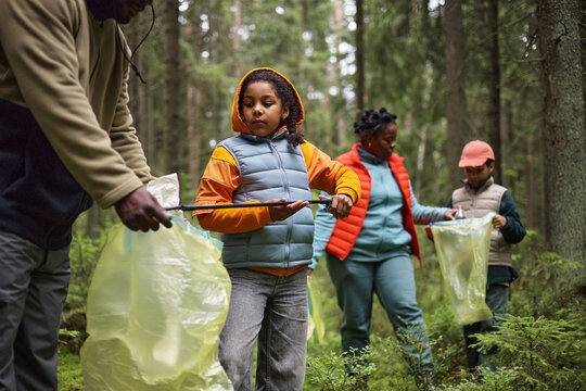 African American family collecting litter in forest, holding trash bags and picking up garbage together during cleanup