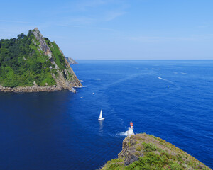 A sailboat rocks lazily at the mouth of Pasaia Bay on the waters of the Bay of Biscay in the Cantabrian Sea, Basque Country.