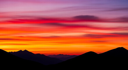 Fototapeta premium Vibrant Sunset Hues Over Silhouetted Mountain Peaks