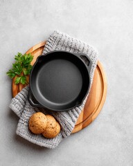 Black cast iron skillet on gray knit cloth and wood round, with parsley and two cookies on a concrete background