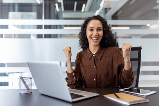 Happy professional celebrating achievement in a modern office workspace with a laptop
