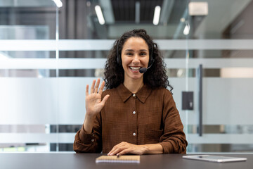 Smiling customer service representative waving during a video call in the office