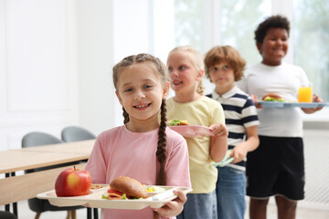 Little kids with trays of tasty food in school canteen, selective focus