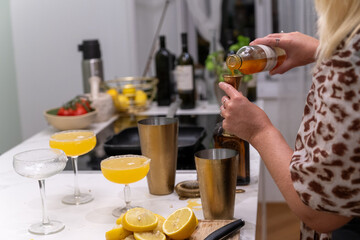 A woman prepares margarita cocktails in a modern kitchen, using fresh lemons, golden shakers, and elegant glassware for a vibrant home experience.