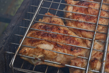 Juicy pieces of chicken are grilled in a metal grill over hot coals. The ruddy crust and smoky aroma emphasize the atmosphere of a picnic and a summer vacation in nature.