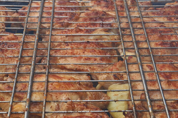 Juicy pieces of chicken are grilled in a metal grill over hot coals. The ruddy crust and smoky aroma emphasize the atmosphere of a picnic and a summer vacation in nature.