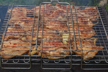 Juicy pieces of chicken are grilled in a metal grill over hot coals. The ruddy crust and smoky aroma emphasize the atmosphere of a picnic and a summer vacation in nature.