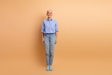 Fototapeta premium Charming Stylish Mature Woman Poses in Casual Fashion on Beige Background