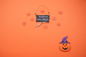 Fototapeta premium Cheerful Halloween flat lay: 'Happy Halloween' wooden sign with carved pumpkins and a witch hat pumpkin on a vibrant orange background. Perfect for festive autumn