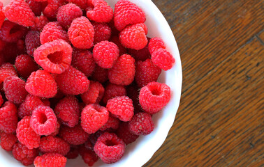 Plate filled with freshly picked raspberry berries on a rough wooden table copy space stock image 
