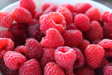 Ripe bright raspberries in a small white bowl close up stock photo. Domestic berries harvest detailed photo 