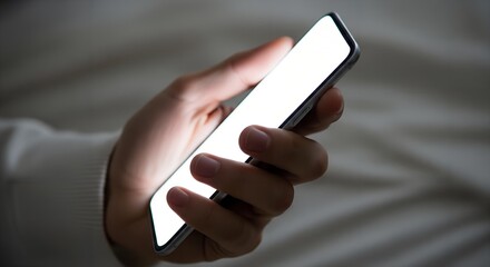 Close-up shot of a hand holding a smartphone mockup with a bright blank screen in low light, showcasing a clean, minimalist aesthetic.