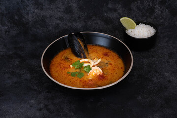 A colorful and vibrant seafood soup that is served with steaming rice and a tangy lime, ideal for food lovers on black background.