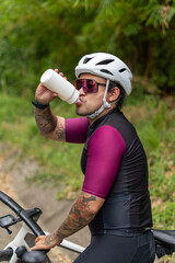 Naklejka premium Vertical shot of male cyclist drinking water during a ride in the forest