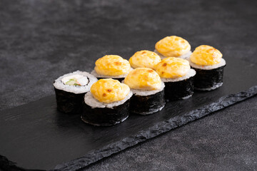 A colorful assortment of sushi rolls, topped with creamy sauces, served elegantly on a dark slate plate.