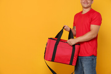 Food delivery service. Courier with thermo bag on orange background, closeup. Space for text