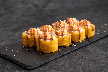 Savor and enjoy these beautifully arranged, deliciously crispy sushi rolls topped with savory ingredients on black board.