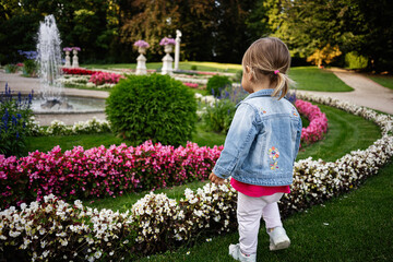 Young child exploring a vibrant garden with flowers and fountain in Lancut, Poland