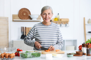 Senior woman cooking at white marble table in kitchen