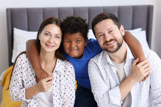 Adoption. Happy parents and their son on bed at home