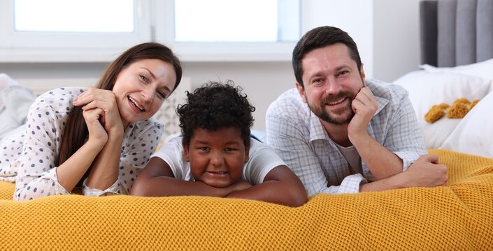 Adoption. Happy parents and their son on bed at home