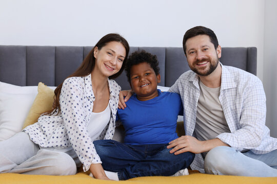 Adoption. Happy parents and their son on bed at home