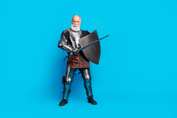 Naklejka premium Senior man in medieval knight armor holding shield and sword, placed against blue background