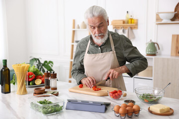 Elderly man cooking at white marble table in kitchen