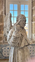 Ancient stone angel statue with detailed wings and robe inside a historic European building, symbolizing religious art, cultural heritage, and spiritual devotion in classical architecture