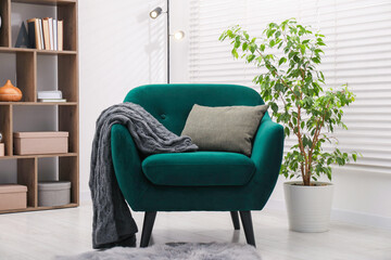 Stylish armchair with pillow and blanket indoors. Interior design
