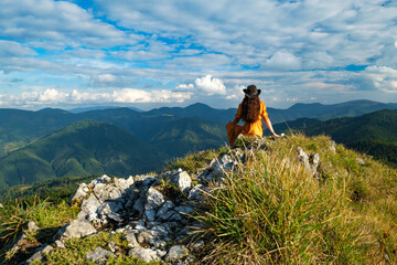 Woman in yellow dress with hat sitting on top of mountain.