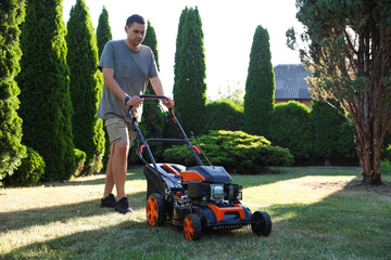 Man cutting green grass with lawn mower in garden
