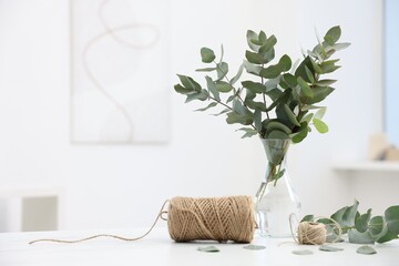 Florist. Eucalyptus branches in vase and threads on white table in flower shop, space for text © New Africa