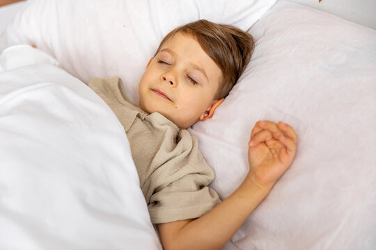 Cheerful little boy sleeping under white blanket in bed. Child woke up with a good mood in the morning. textiles for the nursery. Have a nice day. Motherhood concept. High quality photo. Copy space - Powered by Adobe