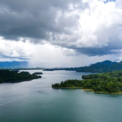 Obraz premium Dramatic clouds gather over a tranquil lake, surrounded by lush green islands and mountains.